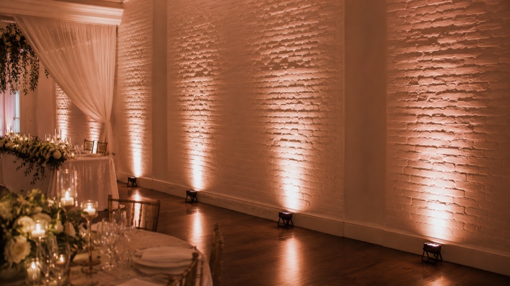 Warm wireless uplighting washing a venue wall in amber
