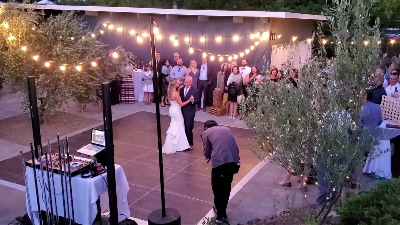 An outdoor wedding first dance under string lights with the DJ booth nearby