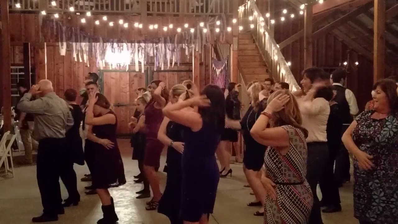 A packed barn wedding dance floor under warm string lights
