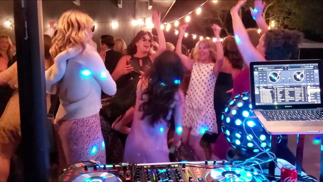 A wedding DJ at the booth with a packed dance floor under string lights