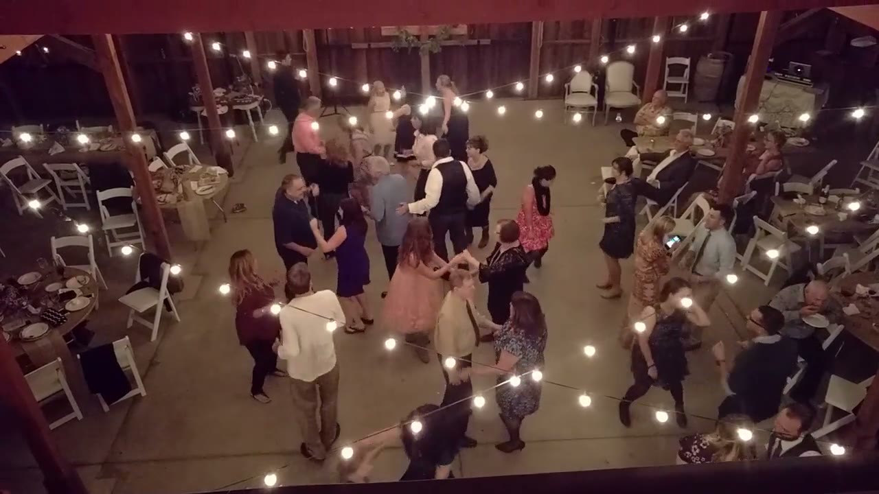 Guests dancing in a circle of string lights at a barn wedding reception