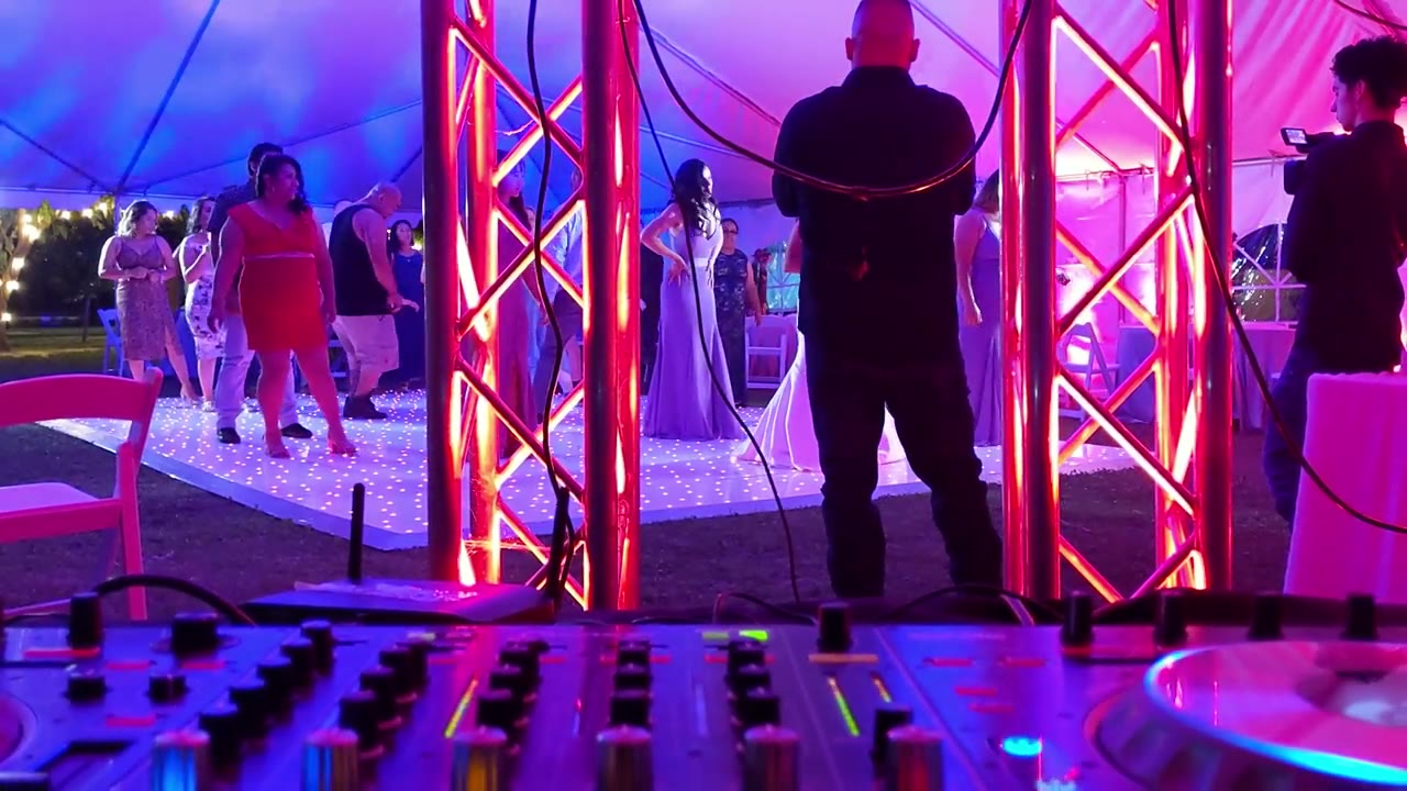 A wedding DJ booth at a tented reception glowing with purple uplighting